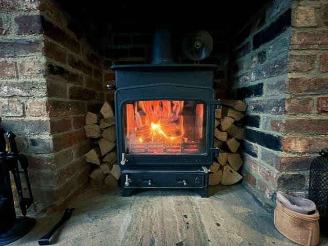 Black wood stove burning in a brick alcove with stacked firewood
